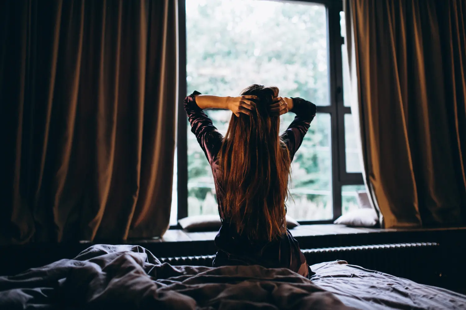 Mujer en la cama frente a la ventana recibiendo la luz natural de la mañana en un dormitorio